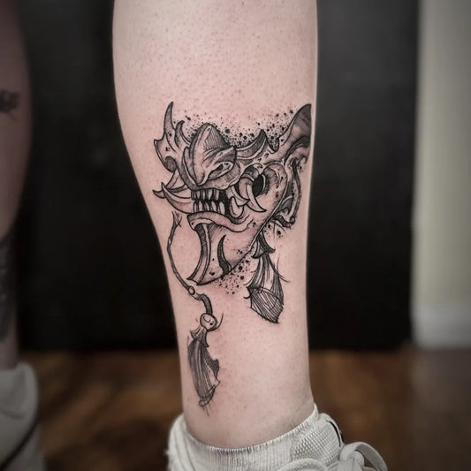Medium Blackwork Oni Mask with Tassel on Women Leg Tattoo by @danrhodestattoo
