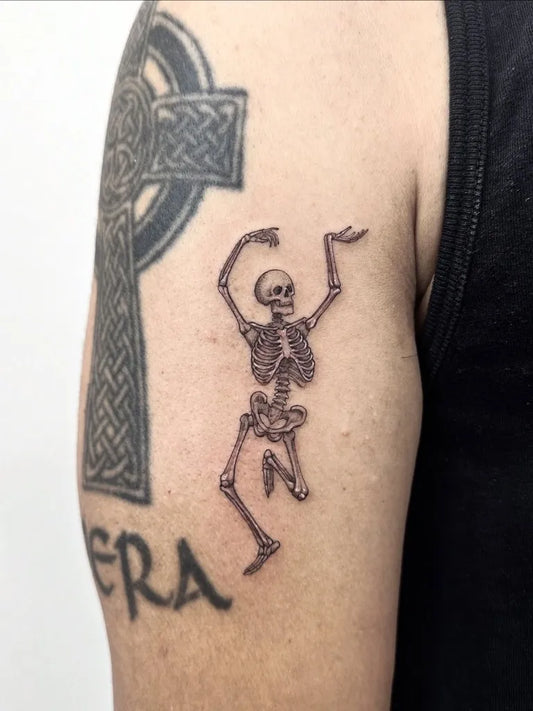 Medium Blackwork Skeleton and Celtic Cross Tattoo on Men Upper Arm by @cendra_studio