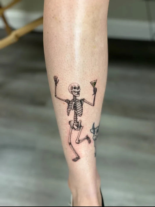 Medium Blackwork Skeleton with Champagne Glasses Tattoo on Women Leg by @rhi.tattoos