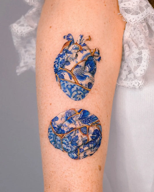 Medium Blue Broken Porcelain Heart and Brain Tattoo on Women Arm by @e.nal.tattoo