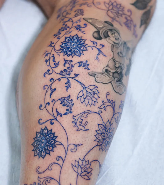 Medium Blue Mickey Mouse and Lotus Flowers Tattoo on Women Thigh by @swanissober