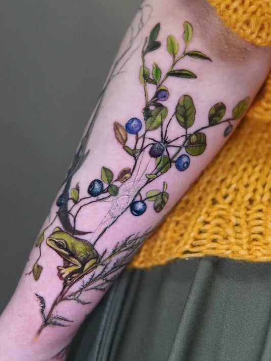 Medium Illustrative Frog and Blueberry Branch Tattoo on Women Arm by @kotyns