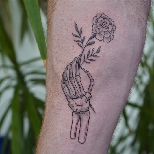 Medium Linework Skeleton Hand Holding Marigold Flower Tattoo on Men Forearm by @morningglorytattoos