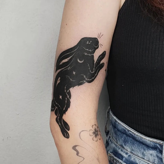 Medium Negative Space Jumping Rabbit Tattoo on Women Arm by @blackolive.tattoo