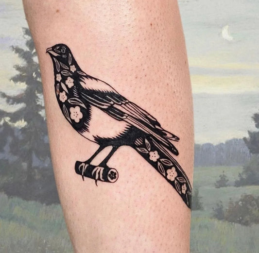 Medium Negative Space Magpie with Flowers Tattoo on Women Leg by @hemlocktattoostudio