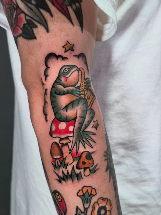 Medium New School Frog Playing Saxophone on Mushroom Tattoo on Men Arm by @tattoopaulski