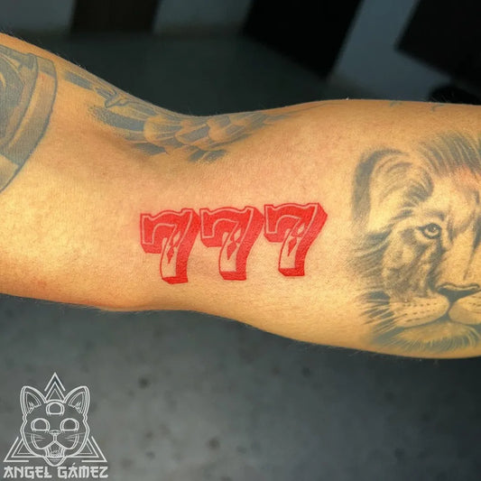 Medium Red Ink 777 and Lion Tattoo on Men Arm by @gamez.tattoo