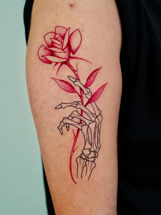 Medium Red Rose and Skeleton Hand Tattoo on Women Arm by @miseria.ttt