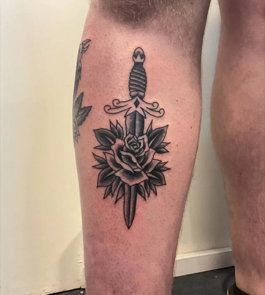 Medium Traditional Dagger and Rose Tattoo on Men Leg by @believe_steve_tattoo