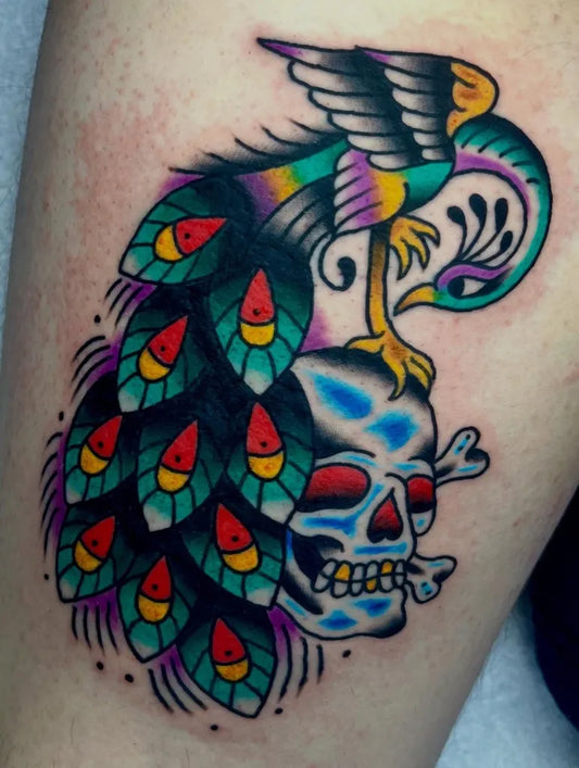 Medium Traditional Peacock and Skull Tattoo on Men Thigh by @anchoredaweightattoo