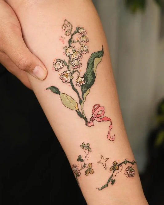 Medium Watercolor Lily of the Valley with Ribbon and Flowers on Women Arm Tattoo by @momo.tattooist