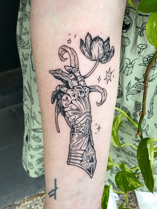 Medium Woodcut Skeletal Hand Holding Lotus Flower Tattoo on Women Forearm by @silly_little_tattooist
