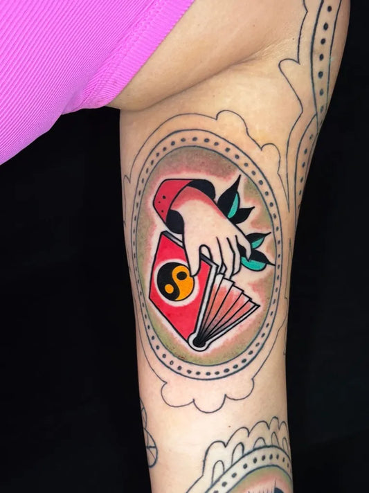 Small American Traditional Hand Holding Yin Yang Fan on Women Arm Tattoo by @flowkappatattoo