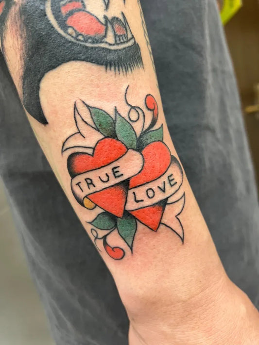 Small American Traditional Two Hearts with Banner and Leaves on Men Forearm Tattoo by @we_love_rose_company
