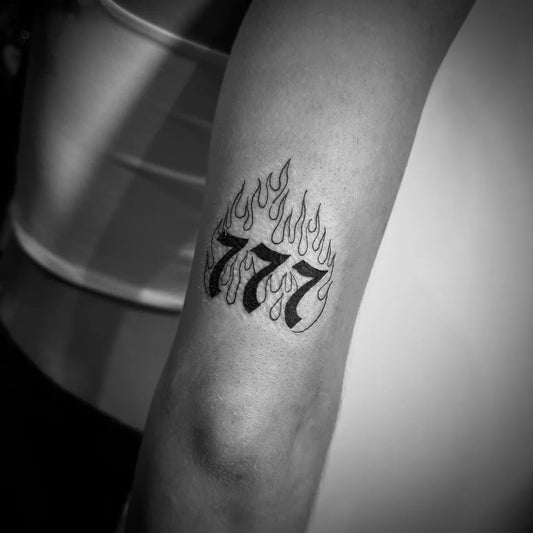 Small Black and Grey 777 with Flames Tattoo on Women Arm by @ipobolu.tattoo