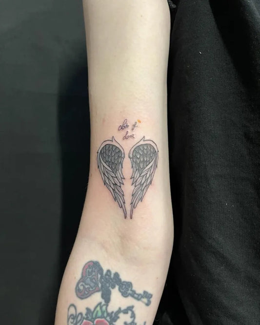 Small Black and Grey Angel Wings Tattoo on Women Arm by @grimmyink.tattoos