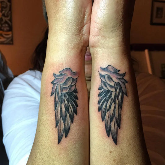 Small Black and Grey Angel Wings Tattoo on Women Wrists by @burningsparrowtattoo