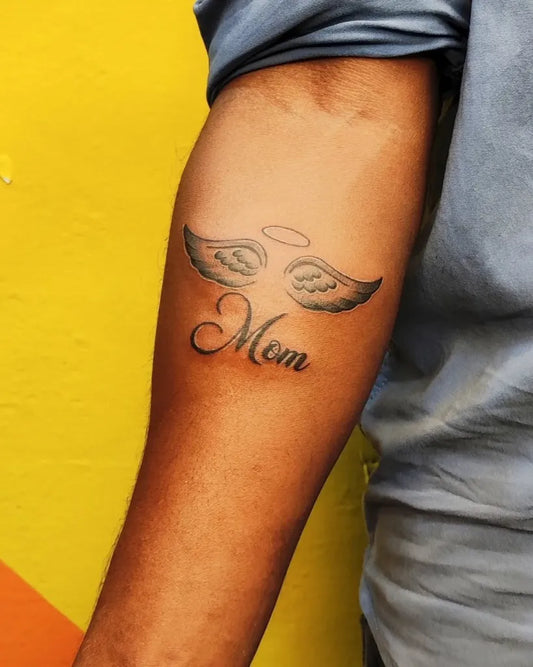 Small Black and Grey Angel Wings and Mom Tattoo on Men Arm by @praveen_ink_