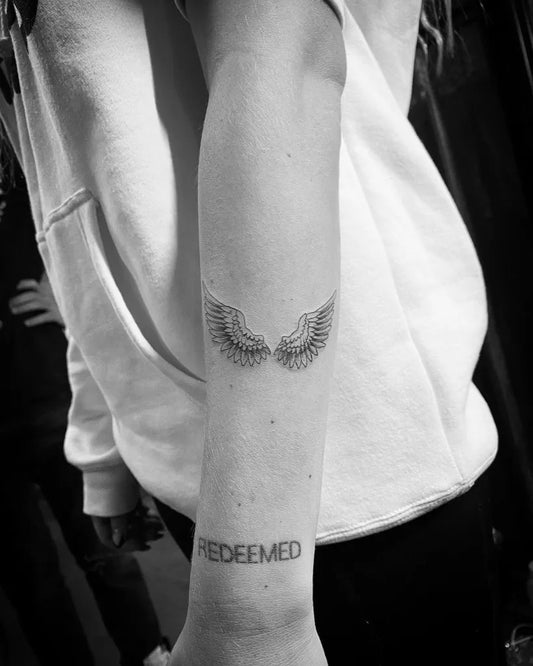 Small Black and Grey Angel Wings and Redeemed Tattoo on Women Forearm by @al_bustillos