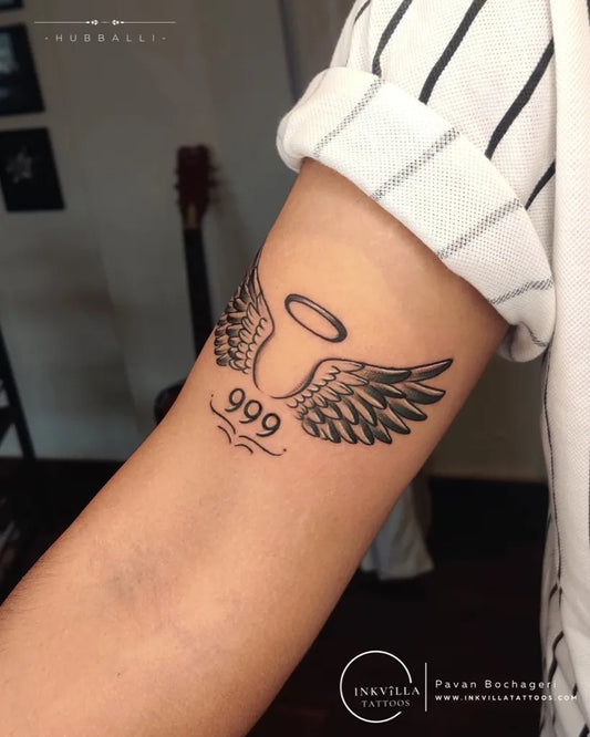 Small Black and Grey Angel Wings with Halo and 999 Tattoo on Women Arm by @inkvilla_tattoos_hub