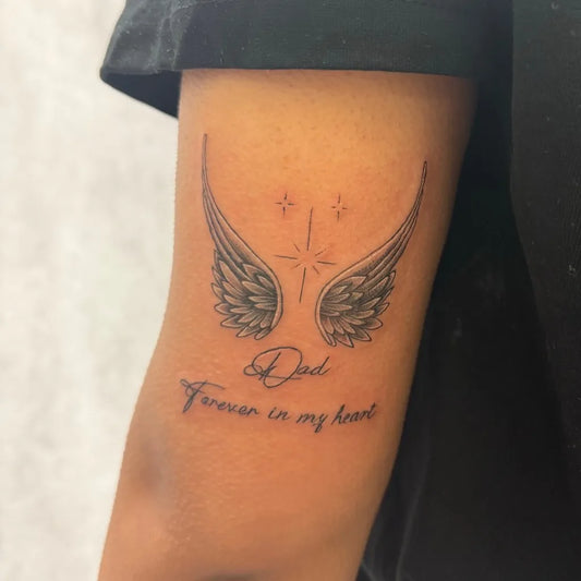 Small Black and Grey Angel Wings with Stars and Text Tattoo on Women Arm by @inkspirehouse
