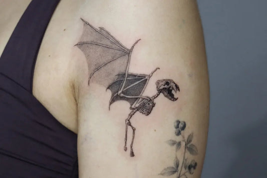 Small Black and Grey Bat Skeleton with Blueberry Branch Tattoo on Women Upper Arm by @kayatatt