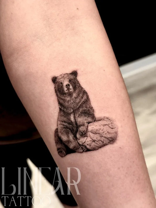 Small Black and Grey Bear on Rock on Women Arm Tattoo by @christina.lineartattoo