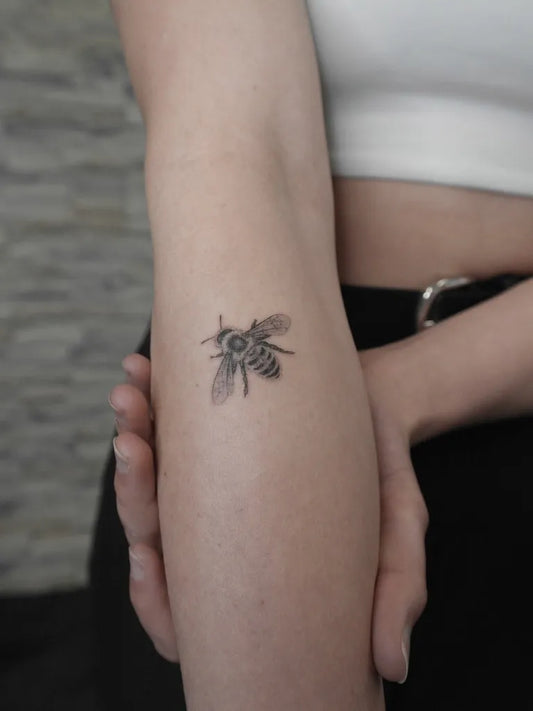 Small Black and Grey Bee on Women Arm Tattoo by @ddianatattoo