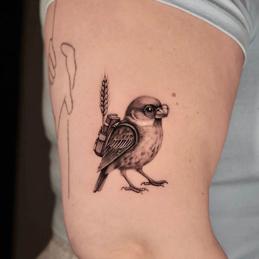 Small Black and Grey Bird with Backpack and Wheat Tattoo on Women Arm by @didow.ink