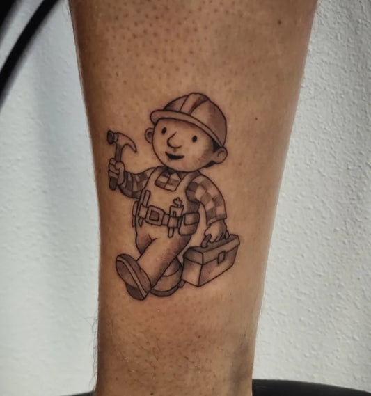 Small Black and Grey Bob the Builder Cartoon Tattoo on Men Leg by @rubenmartinstattoos