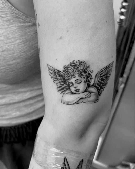 Small Black and Grey Cherub Tattoo on Women Arm by @ruthie_tattoo