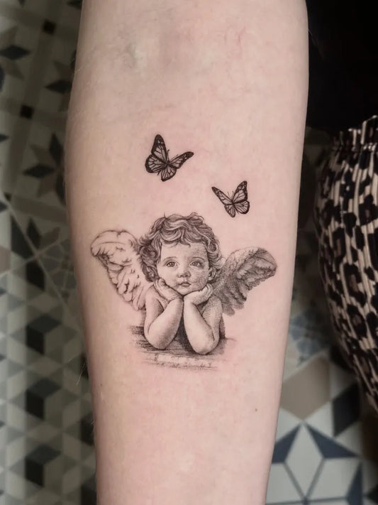 Small Black and Grey Cherub and Butterflies Tattoo on Women Arm by @tattoobycoco