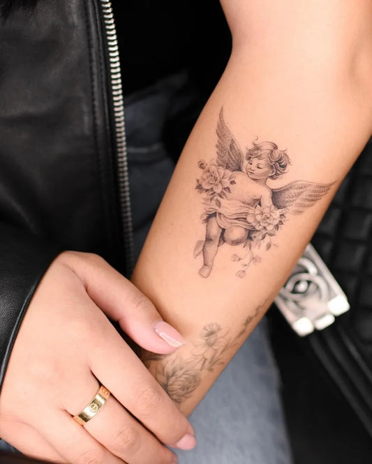 Small Black and Grey Cherub and Flowers Tattoo on Women Arm by @bryan.gee