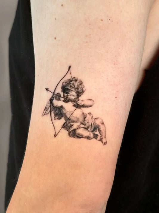 Small Black and Grey Cherub with Bow Tattoo on Women Arm by @keana.6tattoo