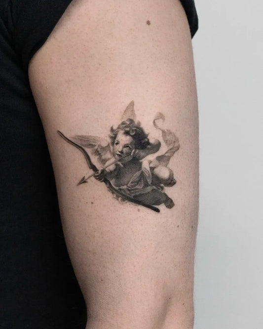 Small Black and Grey Cherub with Bow Tattoo on Women Arm by @lemontreeink