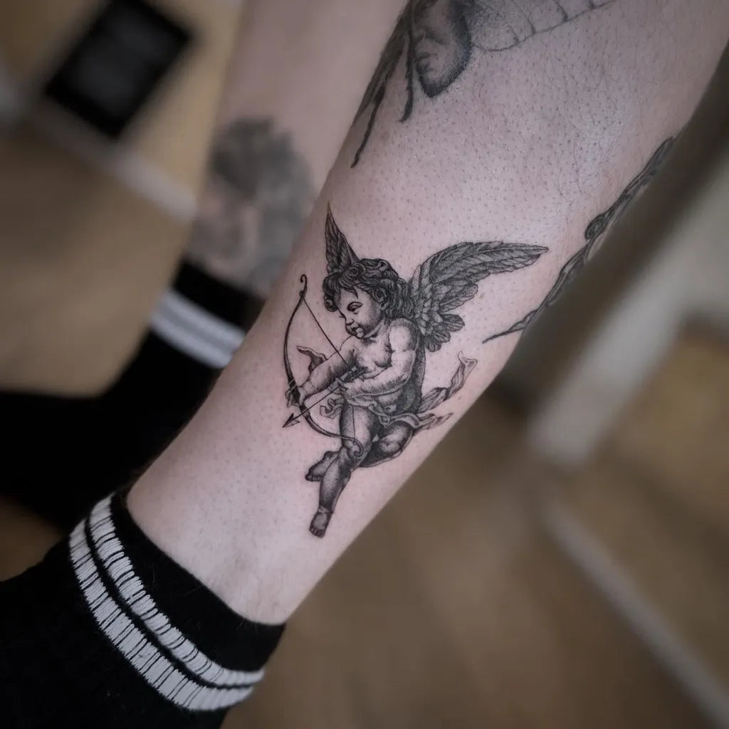 Small Black and Grey Cherub with Bow Tattoo on Women Thigh by @tattoosbyshannen.cass