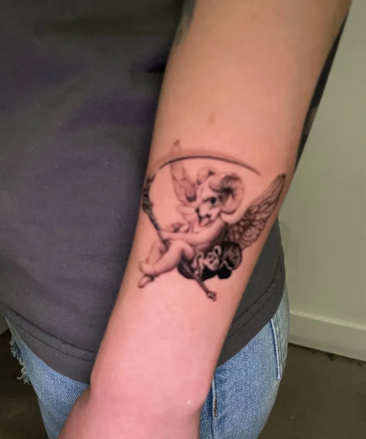 Small Black and Grey Cherub with Scythe and Wings Tattoo on Women Arm by @sayhello.ink