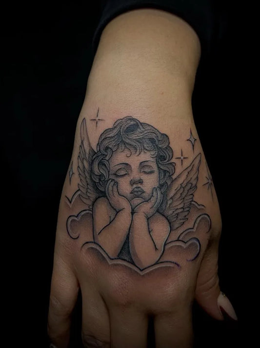 Small Black and Grey Cherub with Wings and Clouds Tattoo on Women Hand by @_.tatsbyaj