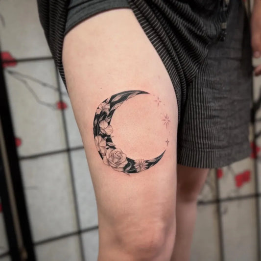 Small Black and Grey Crescent Moon with Flowers Tattoo on Women Thigh by @inkdup.mads