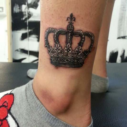 Small Black and Grey Crown Tattoo on Women Ankle by @kimshine_tattoos