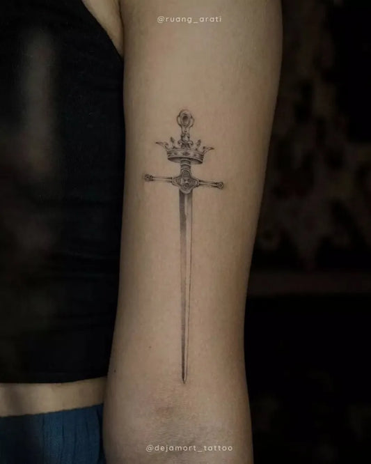 Small Black and Grey Crowned Sword Tattoo on Women Arm by @ruang_arati