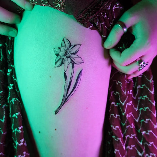Small Black and Grey Daffodil Tattoo on Women Thigh by @jai.d.tattoos