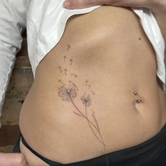 Small Black and Grey Dandelion Tattoo on Women Side by @jochastney.ta