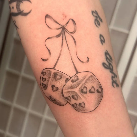 Small Black and Grey Dice with Bow Tattoo on Women Arm by @mayberry.tt