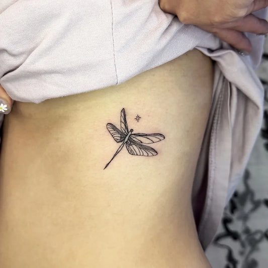 Small Black and Grey Dragonfly with Star on Women Rib Tattoo by @darki.tt.m