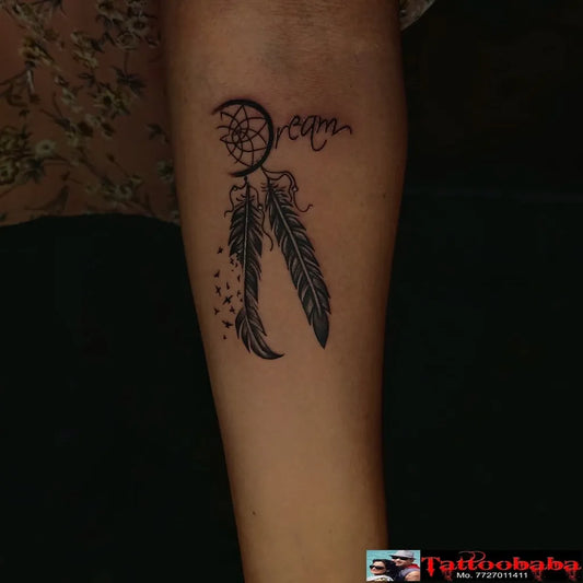 Small Black and Grey Dream Catcher with Feathers Tattoo on Women Arm by @tattoobaba_jaipur