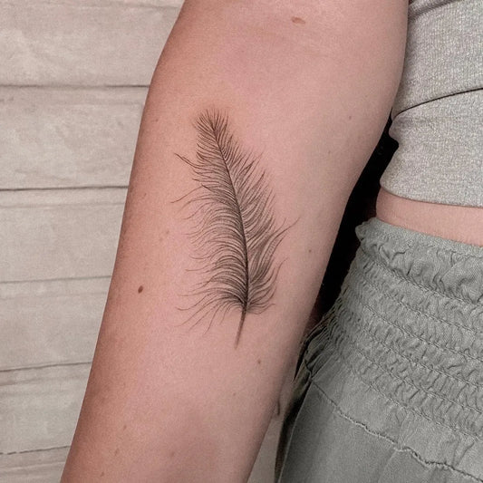 Small Black and Grey Feather Tattoo on Women Arm by @elvis_pachamamatattoo