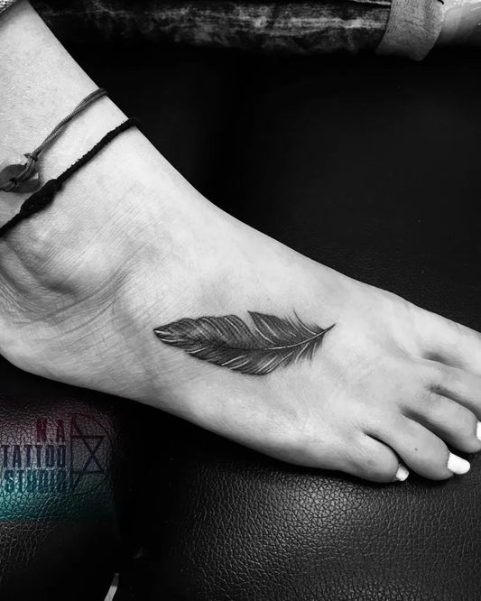 Small Black and Grey Feather Tattoo on Women Foot by @kamayatattoostudio