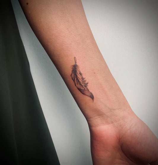 Small Black and Grey Feather Tattoo on Women Forearm by @luzanneink