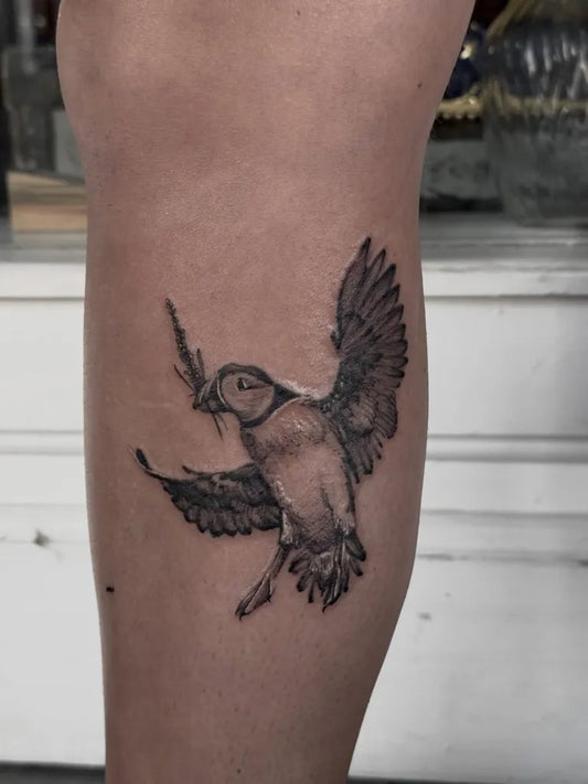 Small Black and Grey Flying Bird with Branch Women Leg by @callmebigchelstattoos
